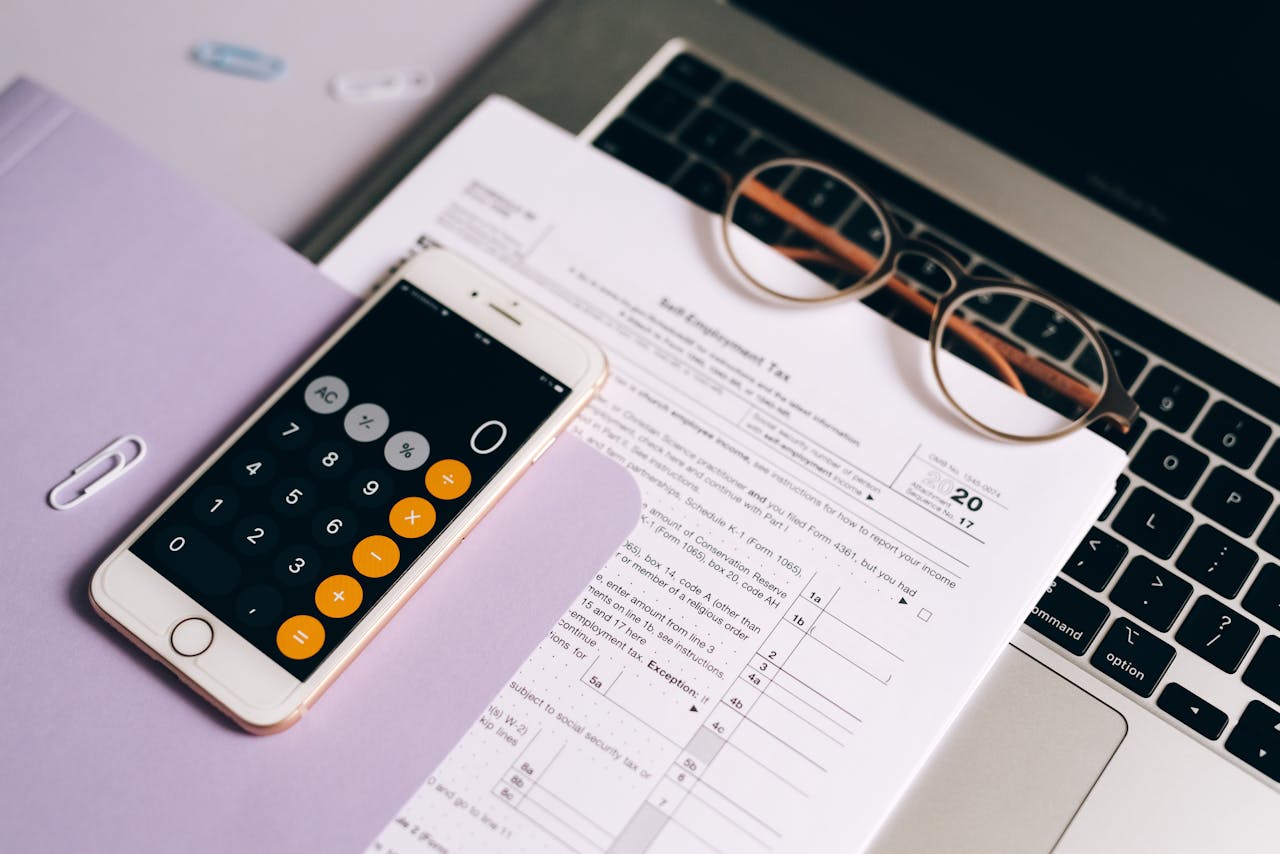 ours-journey A smartphone with a calculator app on tax documents next to a laptop, emphasizing modern accounting.